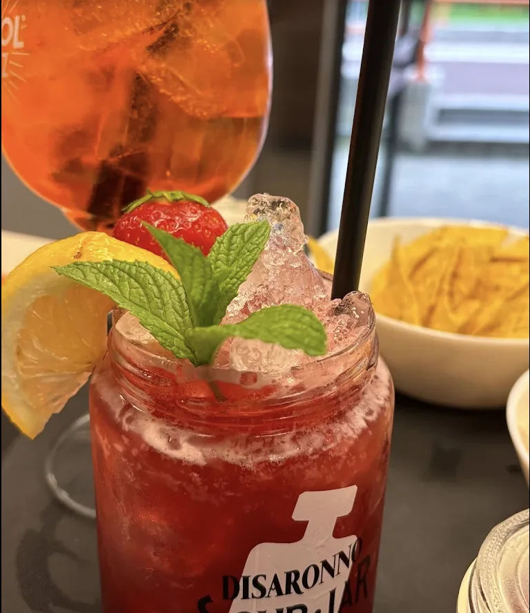 Cocktail rosso guarnito con fragola, limone e menta